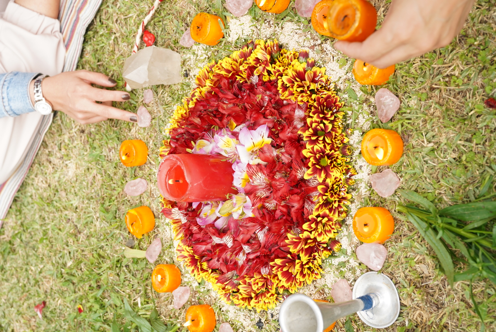 Mandala de flores con vela central y cristales sobre el pasto